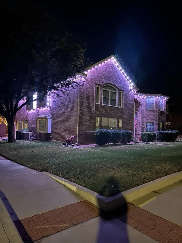 Permanent holiday lighting in pink on a brick corner-lot home in DFW